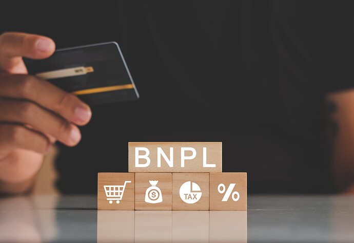 A hand holds a credit card above wooden blocks spelling out 'BNPL' and displaying symbols of shopping, money, tax, and percentage